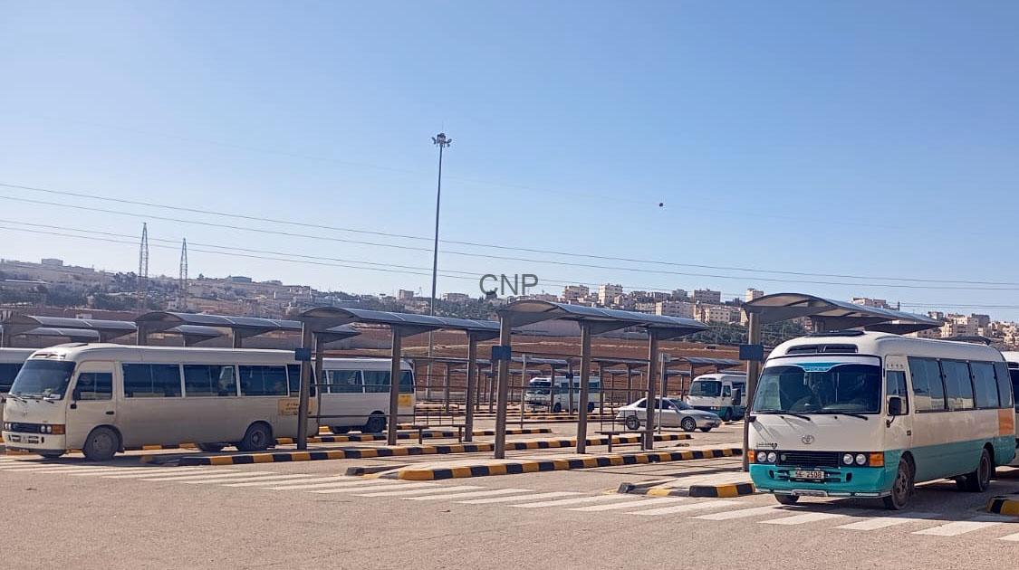 000-10 - Center News Network Bus terminal with several white and turquoise minibuses under sheltered bays; urban skyline in the distance.