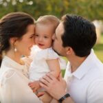 Happy couple kissing their smiling baby outdoors.
