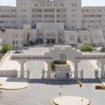 Front view of a government complex with a large curved entrance gate reading 'Ministry of Public Works & Housing' and a circular drop-off area in the foreground.