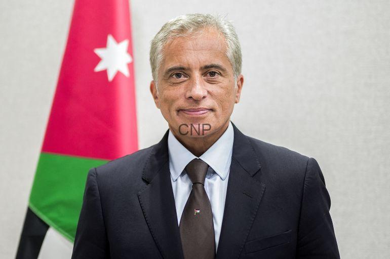 Jaafar-Hassan2-1726579446 - Center News Network Formal portrait of a man in a dark suit and brown tie, with a Jordan flag in the background.