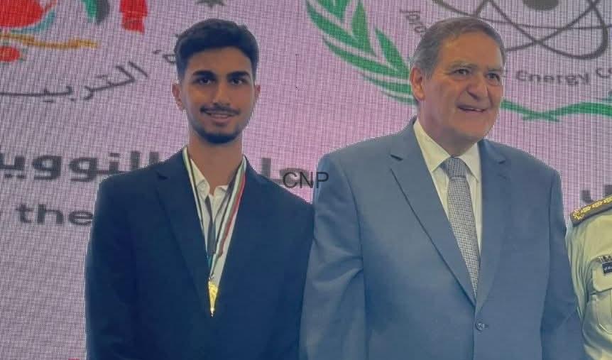 ameen - Center News Network Young man in a dark suit with a gold medal around his neck posing with an older man in a light gray suit on stage at an award ceremony.