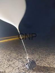 White helium balloon tied to a small rock on a sandy surface, under a dark night sky with a faint road line in the background.