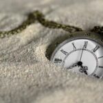 Pocket watch partly buried in sand, chain draped across the surface.