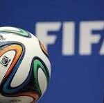 Soccer ball with multicolored panels in front of a blue FIFA backdrop.