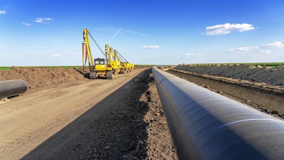 Yellow excavators lay a large underground pipeline along a dirt road under a blue sky, during construction.