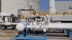 Industrial piping system with valves and gauges at an outdoor facility, mounted on blue supports under a clear sky.