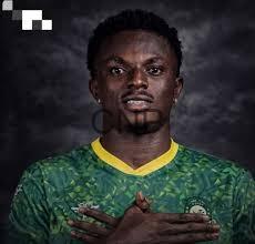 Portrait of a male football player in a green jersey with yellow trim, arms crossed over his chest against a dark cloudy background.
