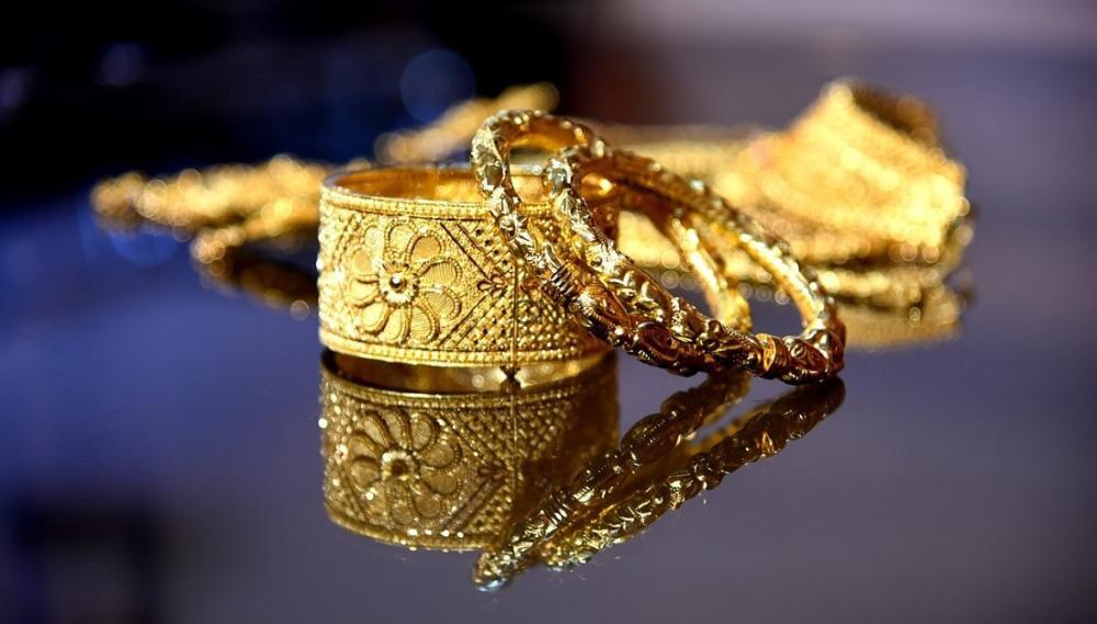Close-up of ornate gold bracelets and rings on a mirrored surface, with floral engravings and reflections.
