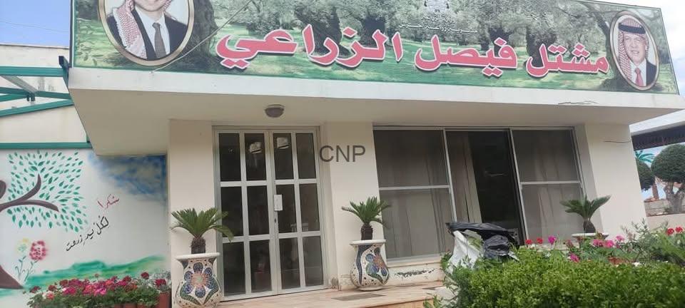 mash - Center News Network Front of a small building with a large Arabic banner featuring portraits, glass doors, and potted palms in front.