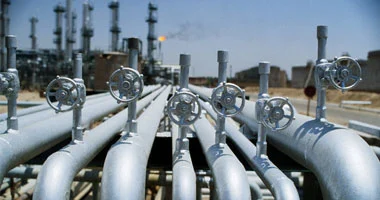 Rows of large metal pipelines with circular valve wheels at an oil refinery or processing plant.