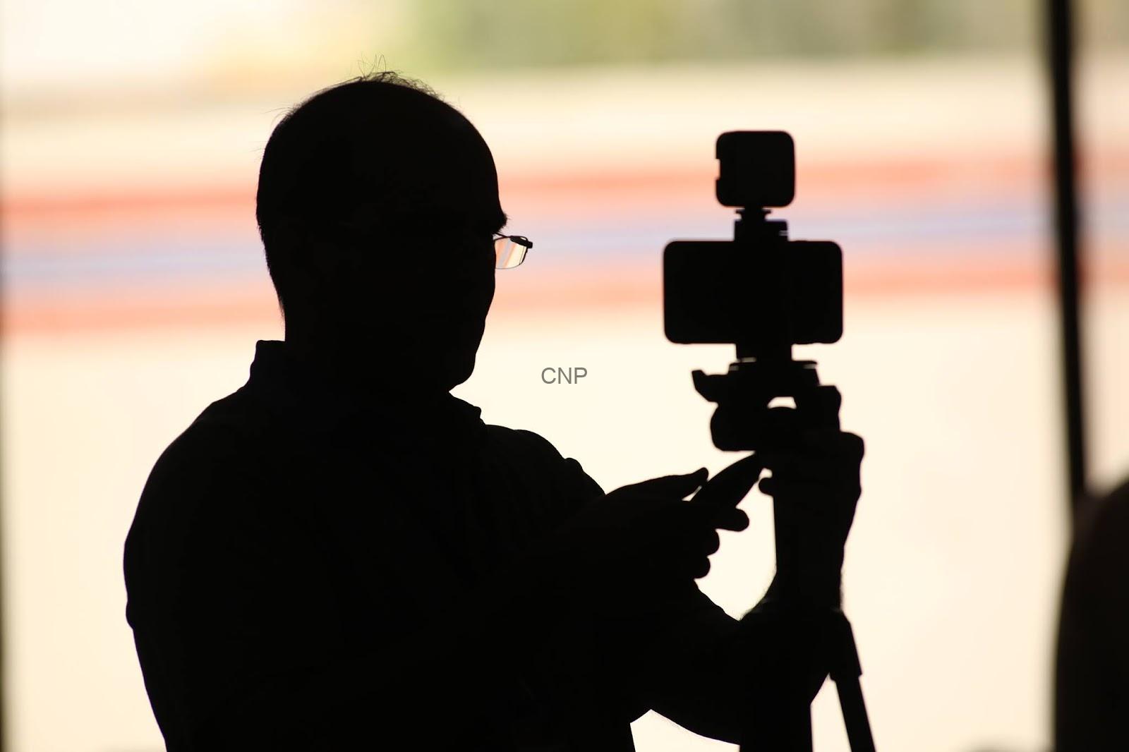 Silhouette of a photographer adjusting a camera on a tripod at sunset.