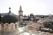 q - Center News Network Aerial view of a historic Middle Eastern city with white stone buildings, domed roofs and minarets seen from above.