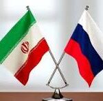 Two small national flags, Iran and Russia, crossed on a flag stand on a desk with a blurred office background.