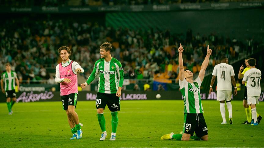 ry - Center News Network Soccer players in green-and-white uniforms celebrate on a bright stadium field, with one kneeling and pointing to the sky as teammates smile nearby.