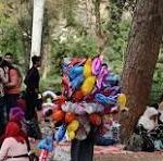 Balloon artist wearing a colorful flower headdress performing in a crowded park.