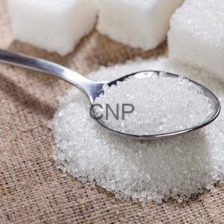Spoon scooping white granulated sugar on a burlap surface with sugar cubes in the background.