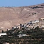 Hilly landscape with a small town of white and beige buildings at the hill’s base, set against a dry, brown hillside.
