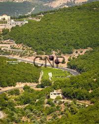 Winding road through a green hillside dotted with white houses and terraced slopes, with distant mountains in the background.