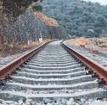 Railroad tracks extend into a hilly landscape with trees on both sides.