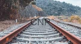 Railroad tracks extend into a hilly landscape with trees on both sides.