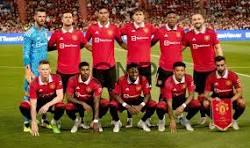Soccer team in red jerseys posing for a group photo on the field with a stadium full of fans behind them.