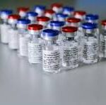 Row of small glass vials with red and blue caps lined up on a sterile lab surface, likely vaccines or medications.