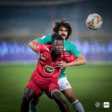 w j - Center News Network Two soccer players battle for the ball in a tight challenge on the field, one in red and one in green.