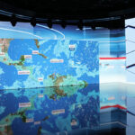 Television news studio with a large blue map screen showing 'CNP' and a professional camera on the right.