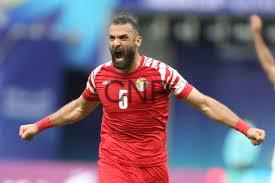 yaz - Center News Network Male footballer in a red kit celebrating with arms outstretched on the pitch.