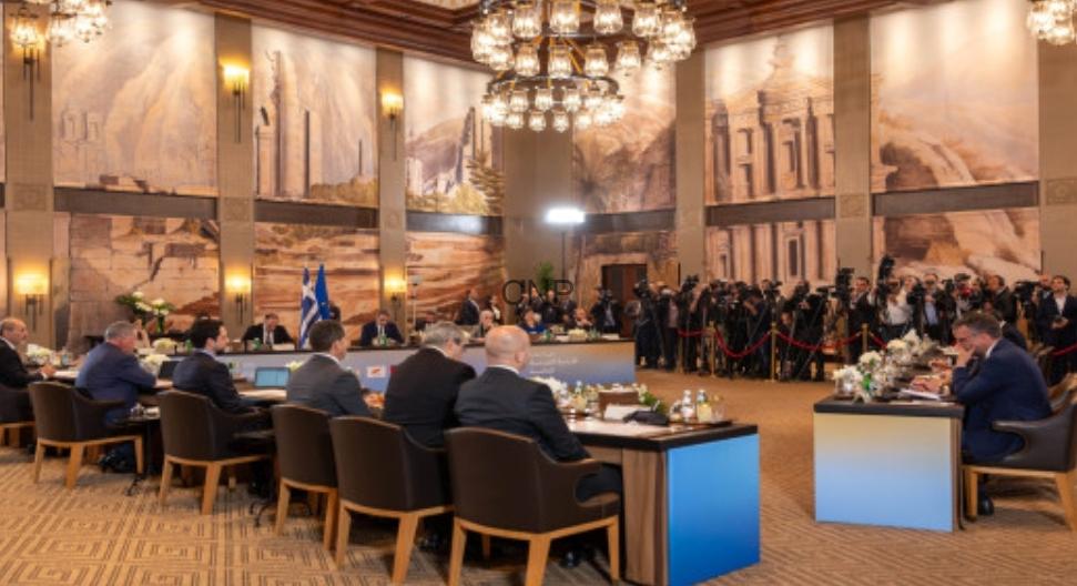 1778073362975 - Center News Network Delegates seated around a U-shaped conference table in a grand hall with murals, chandeliers, and press photographers at the back.