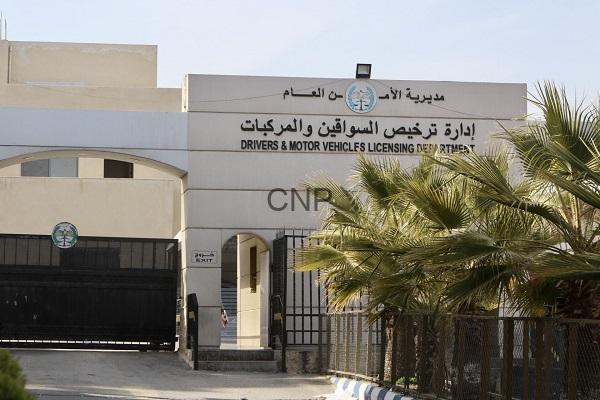 Front view of a government licensing department building with Arabic and English signage, gated entrance, and palm trees nearby.