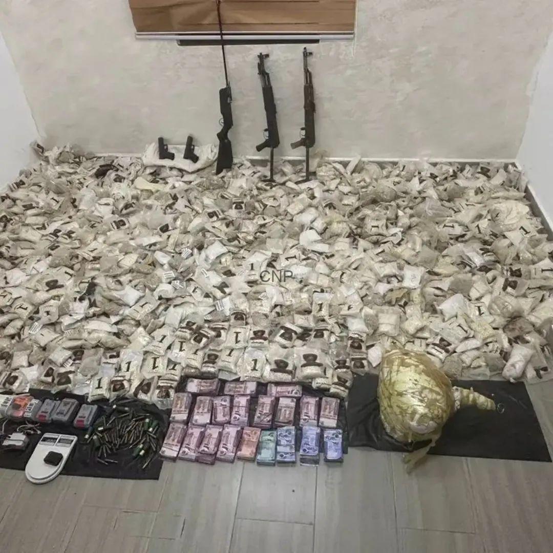 FB_IMG_1778785295962 - Center News Network Rifles propped against the wall with bundled cash, a scale, and ammunition on the floor, implying illicit activity.