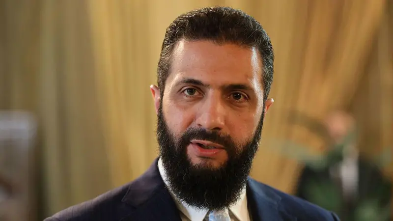 SHAR - Center News Network Man with a dark beard and navy suit looking at the camera in a softly lit room.