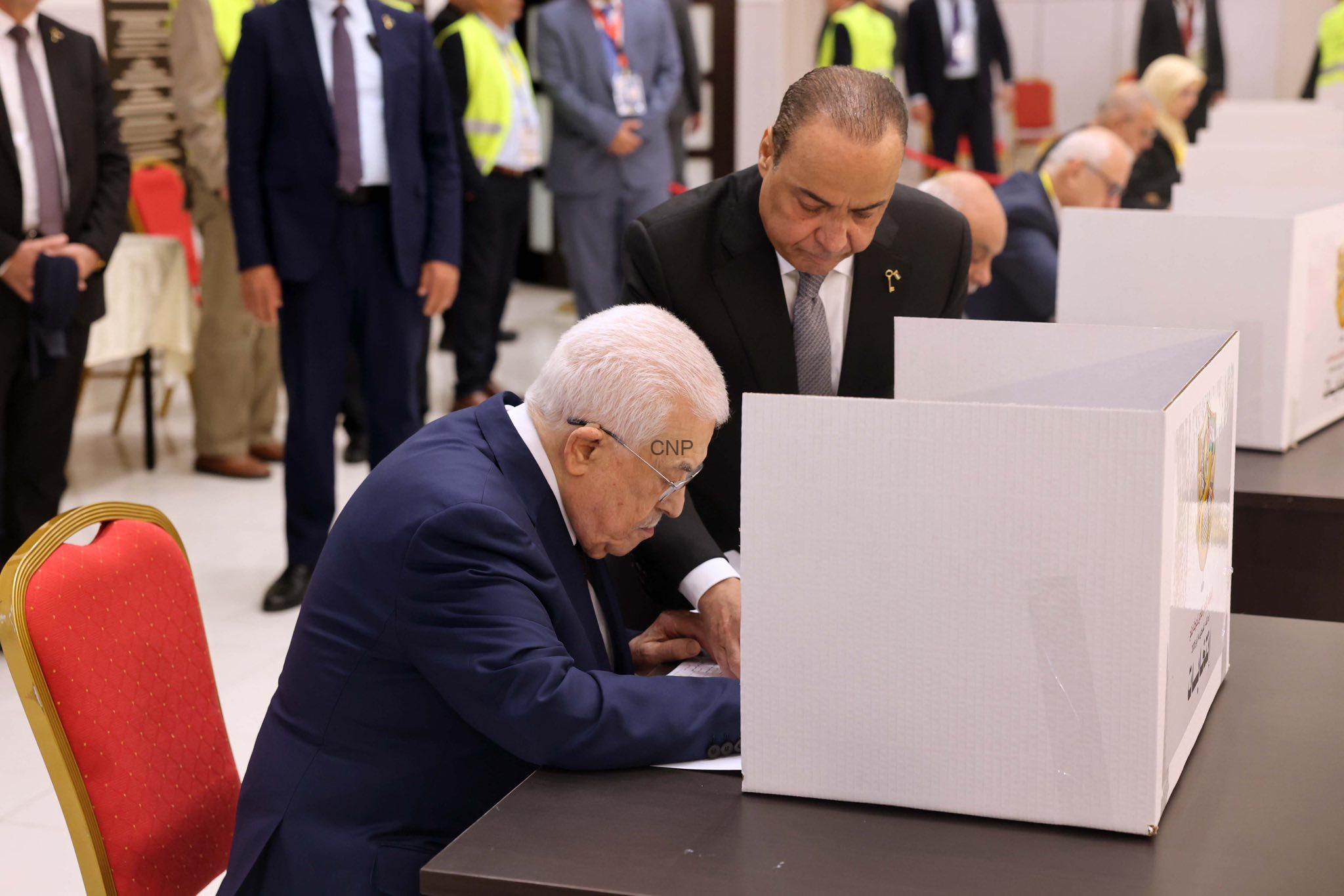 abb - Center News Network Man in a dark suit signing a ballot at a polling booth, with another man overseeing nearby