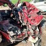 Red car with severe front-end damage from a collision; crumpled hood, exposed engine, and debris on the ground in a crash scene.
