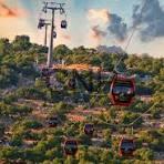Red gondola cable car gliding over a rocky hillside with sparse vegetation and a blue sky.