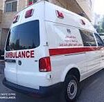 Rear and side view of a white ambulance parked on a city street with red markings and emergency lights visible