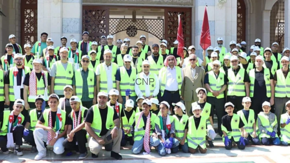 aqa - Center News Network Group photo of volunteers wearing neon safety vests, kneeling and standing in front of a building with red flags in the background.