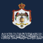 Official government crest on a dark blue background, featuring a crowned shield with an eagle, flags, and Arabic script beneath.