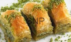bag - Center News Network Close-up of three pistachio baklava pieces on a light surface, showing flaky golden pastry and green chopped pistachios.