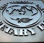 Metal plaque featuring a circular emblem with a globe and a winged symbol, surrounded by large raised lettering. The plaque appears silver on a dark background.