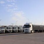 Row of white trucks and trailers parked in a large open lot.