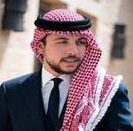 Portrait of a man in a dark suit and tie wearing a red-and-white keffiyeh headscarf, standing outdoors.