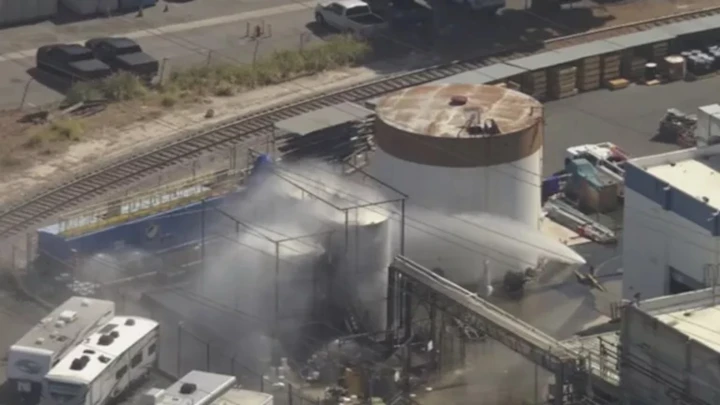 - Center News Network Industrial facility with a cylindrical storage tank and steam venting near rail tracks.