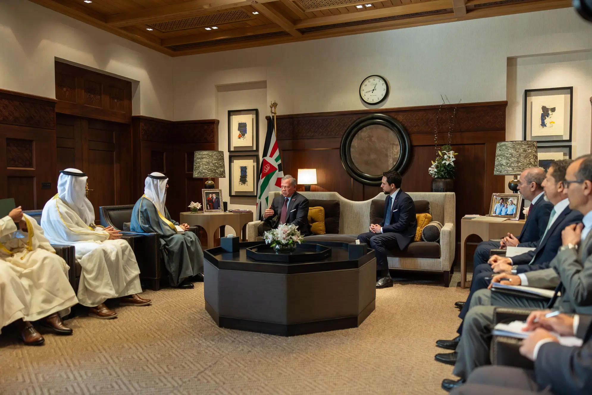 dewan - Center News Network Diplomatic meeting in a wood-paneled room with officials seated in two groups and a Jordan flag nearby, a clock on the wall.