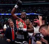 dob - Center News Network Boxer in the ring raising a championship belt in victory, with reporters and photographers around him.