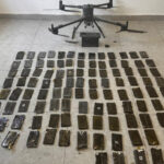 Quadrotor drone on a tiled floor above dozens of black smartphones laid out in a grid as evidence.