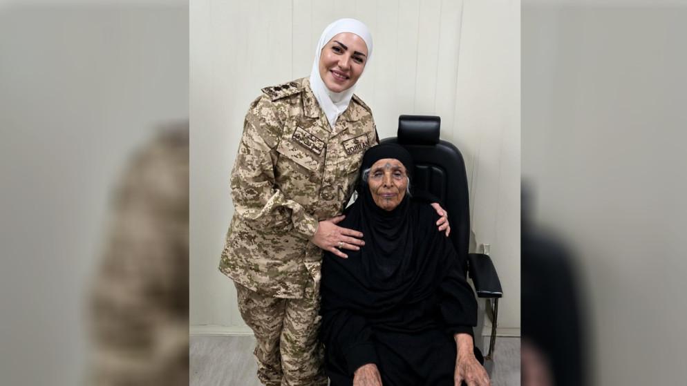 eyes - Center News Network Female soldier in desert camouflage uniform and white hijab stands beside an elderly woman in black seated in a chair, both smiling indoors.
