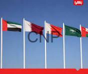 Row of five national flags fluttering on tall flagpoles against a clear blue sky, suggesting an international or diplomatic setting.
