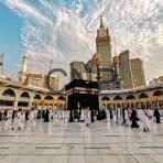 Pilgrims circle the Kaaba in the Grand Mosque in Mecca on a sunny day with clear skies above the courtyard.